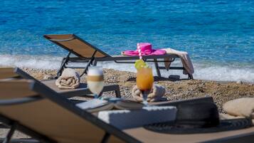 A beachside lounge with sun loungers, a drink, and a hat on the sand.