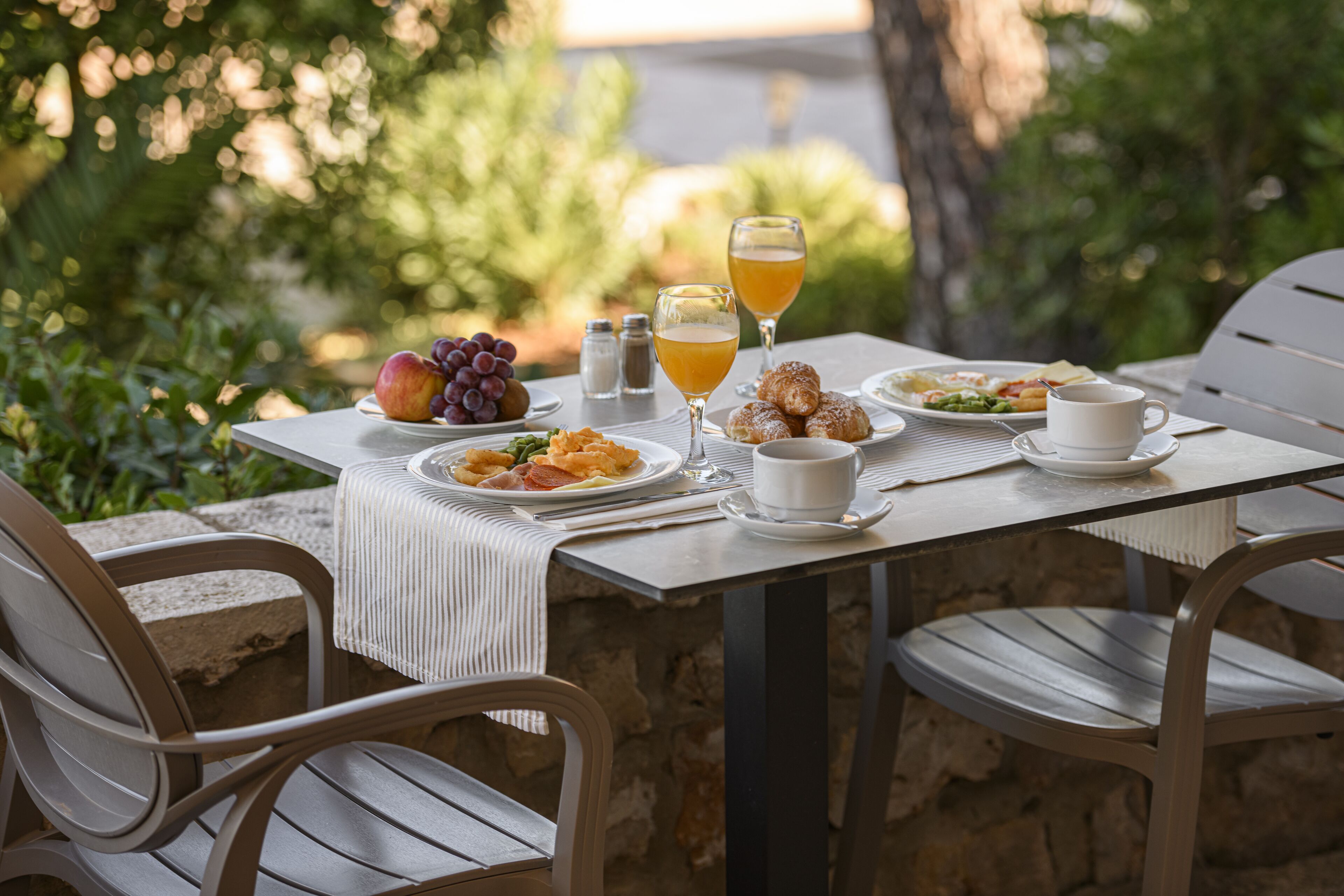 Una mesa para comer al aire libre con platos de comida, vasos de jugo de naranja y una taza de café.