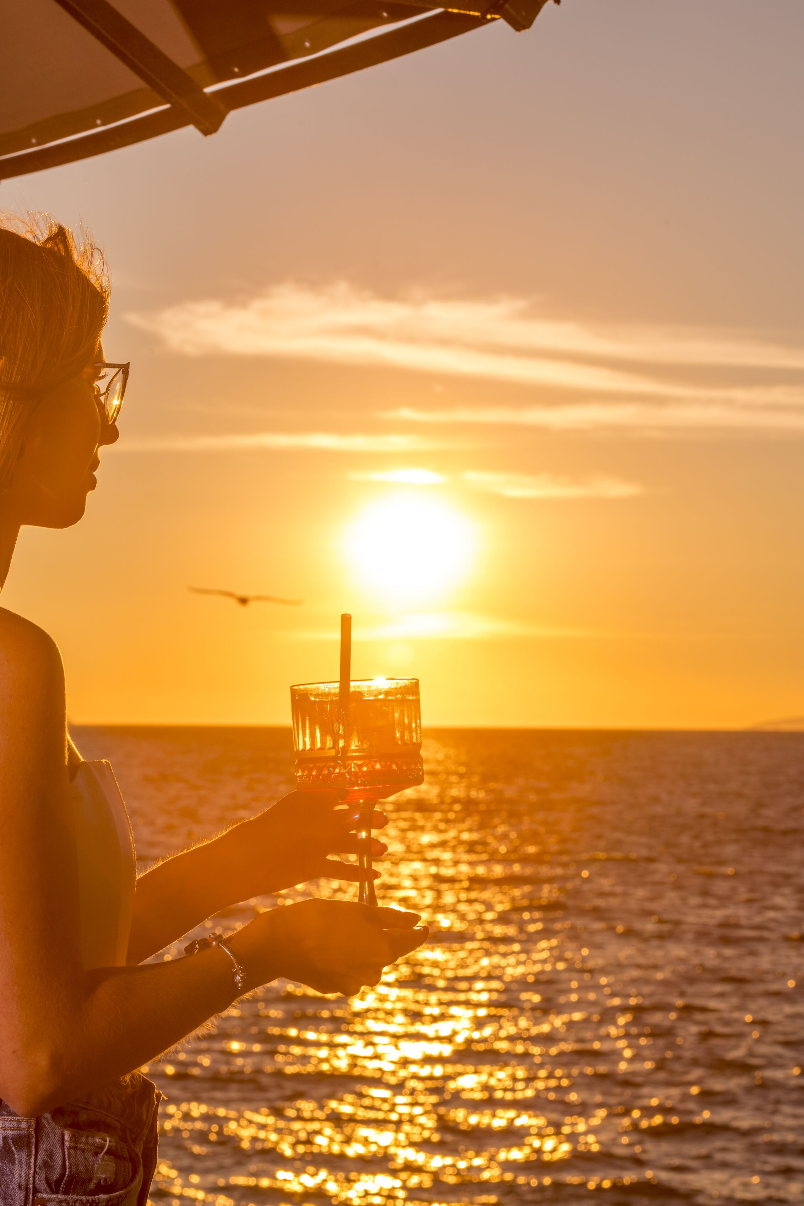 A person holding a drink with a sunset in the background.