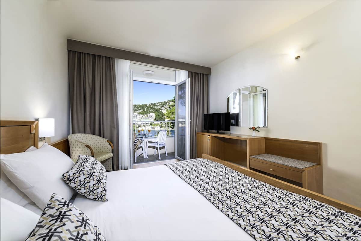 Une chambre d’hôtel comprenant un lit, un bureau, une chaise, une télévision et un balcon avec une table et des chaises.