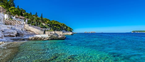 Una zona costera con aguas azules cristalinas, costa rocosa y edificios con escaleras que bajan hacia el agua.