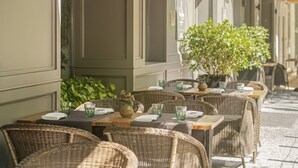 An outdoor café with wicker tables and chairs, green glassware, and a potted plant.