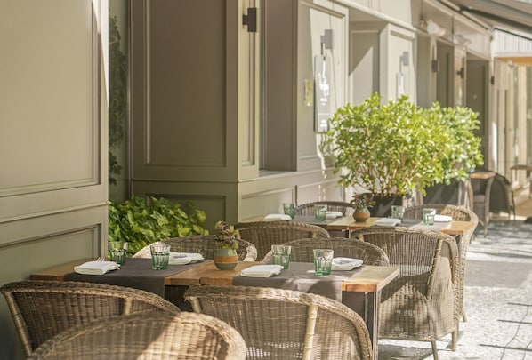 An outdoor café with wicker tables and chairs, green glassware, and a potted plant.