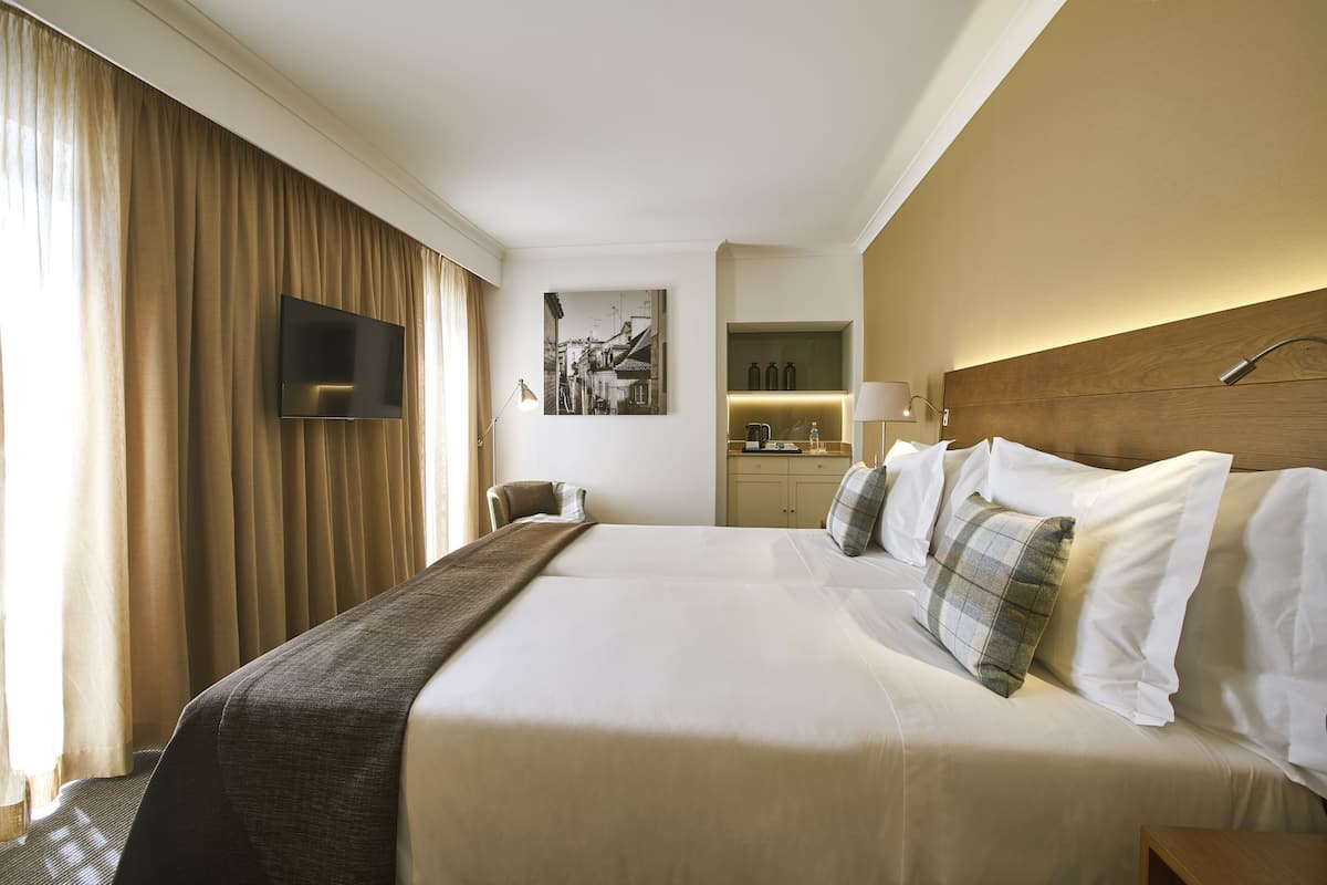Quarto de hotel com uma cama grande, uma televisão de tela plana na parede, uma mesa com abajur e um quadro na parede.