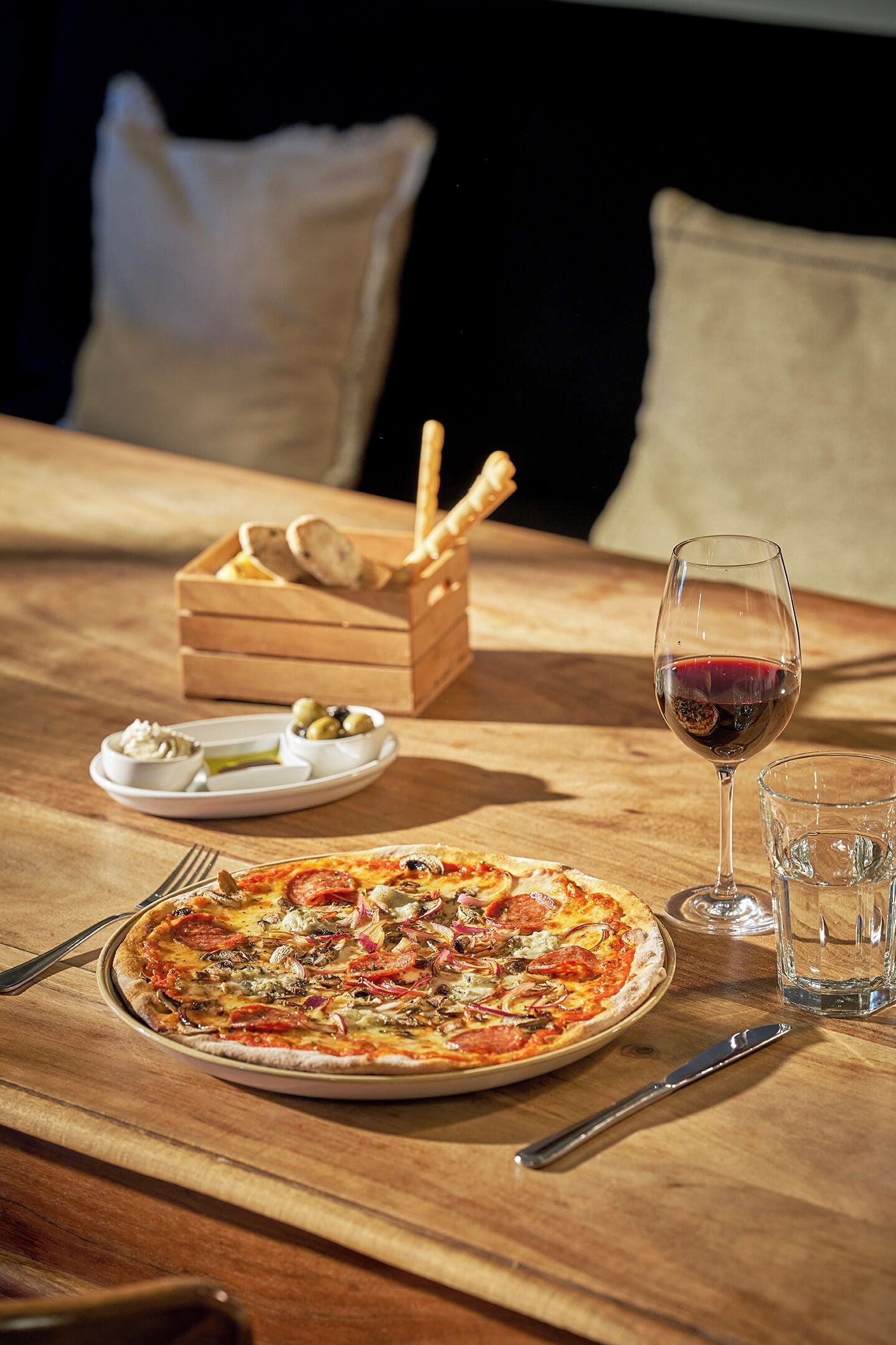 Una mesa de madera con pizza, una copa de vino y una cesta de pan.