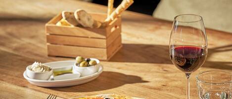 Una mesa de madera con pizza, una copa de vino y una cesta de pan.