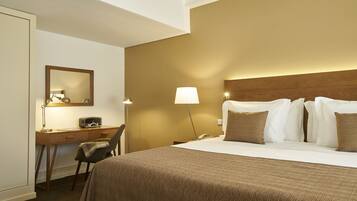 A hotel room with a bed, a desk, a chair, a lamp, and a nightstand.