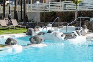 A pool area with lounge chairs, a stone wall, and a white fence. - Hotel LIVVO Anamar Suites (San Bartolomé de Tirajana)