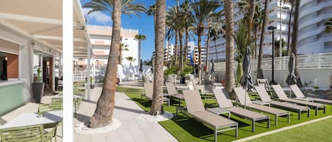 Un complexe hôtelier doté d’un espace extérieur aménagé avec des palmiers et une piscine.