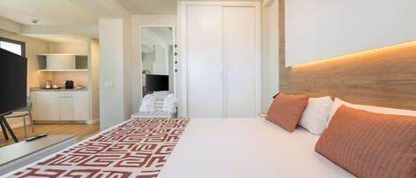 A modern hotel room with a large bed, a TV, a kitchenette, and a bathroom.