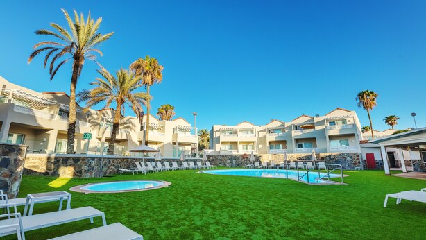 A resort with a swimming pool, lounge chairs, and palm trees. - Apartamentos LIVVO Koala Garden (San Bartolomé de Tirajana)