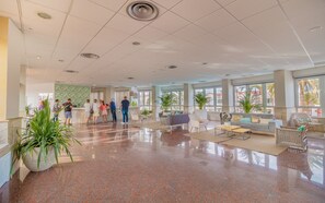 A spacious lobby with a polished granite floor, a reception desk, seating area with sofas and chairs, and large windows offering views of palm trees.