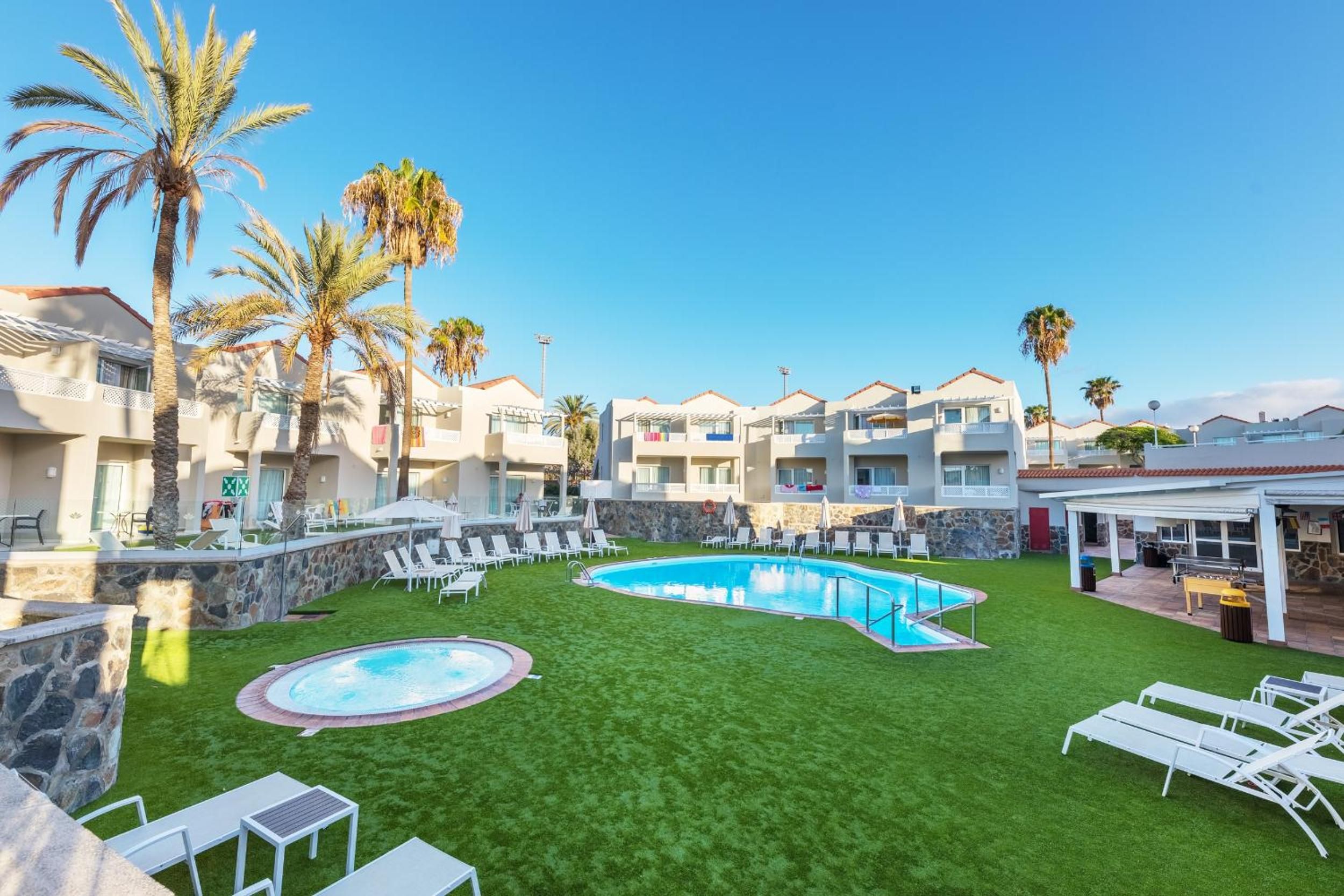 A hotel with a swimming pool, lounge chairs, and palm trees.
