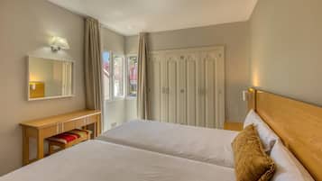Habitación de hotel con dos camas, un banco de madera, un espejo y un armario.