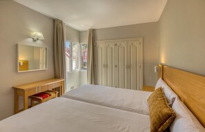A hotel room with two beds, a wooden bench, a mirror, and a wardrobe. - Apartamentos LIVVO Koala Garden (San Bartolomé de Tirajana)