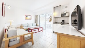 A modern living room with a sofa, a wooden coffee table, and a kitchen area with a microwave and coffee maker. - Apartamentos LIVVO Koala Garden (San Bartolomé de Tirajana)