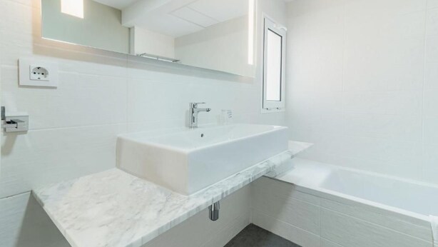 Ein modernes Badezimmer mit einem weißen Waschbecken, einem Spiegel und einer Badewanne.