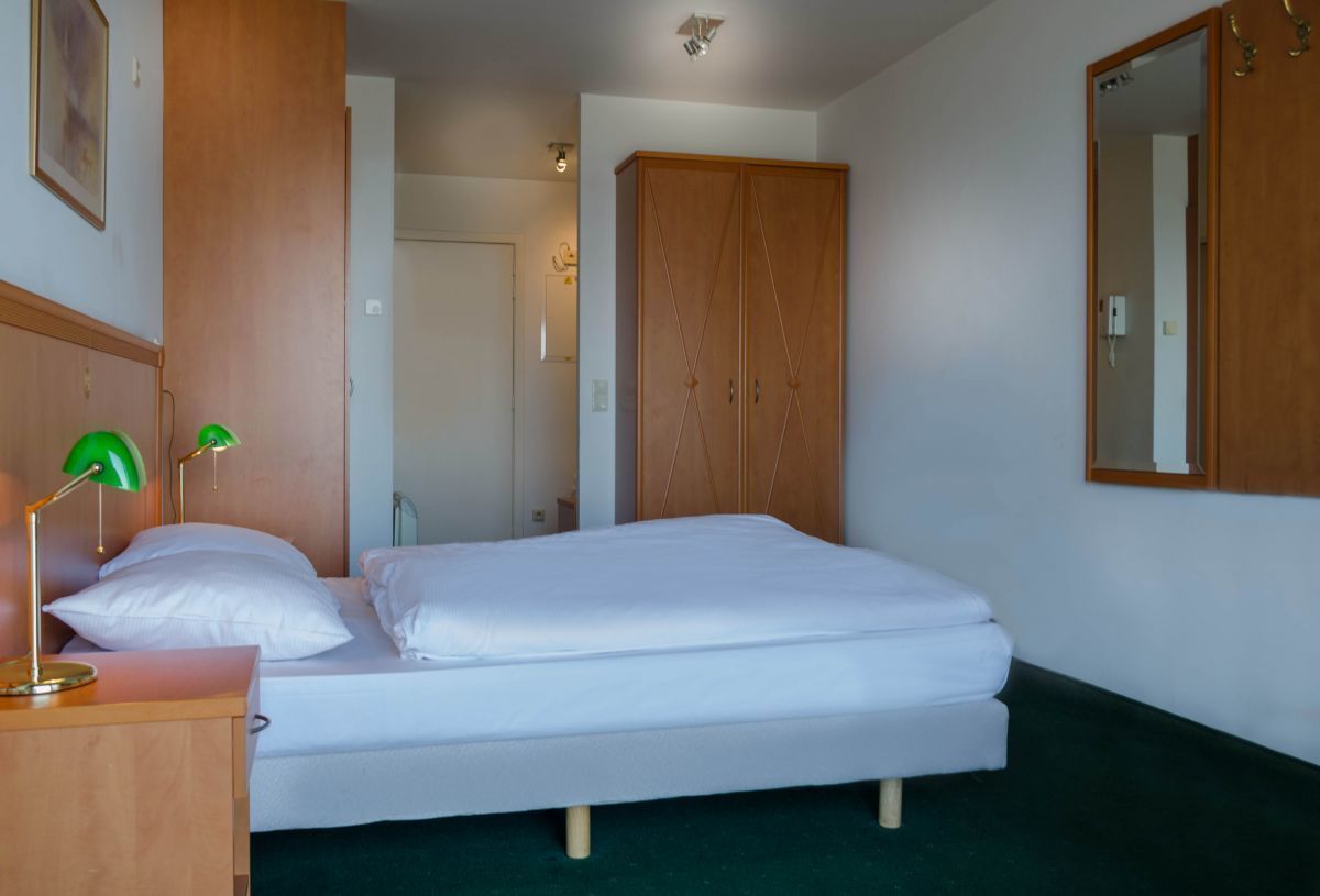 Een slaapkamer met een bed, een houten garderobe, een groene bureaulamp en een spiegel aan de muur.
