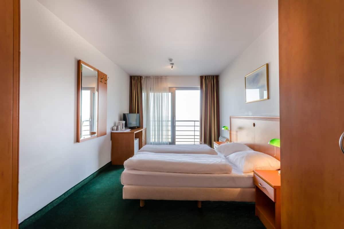 A hotel room with a large bed, a desk with a chair, a television, and a window with curtains.