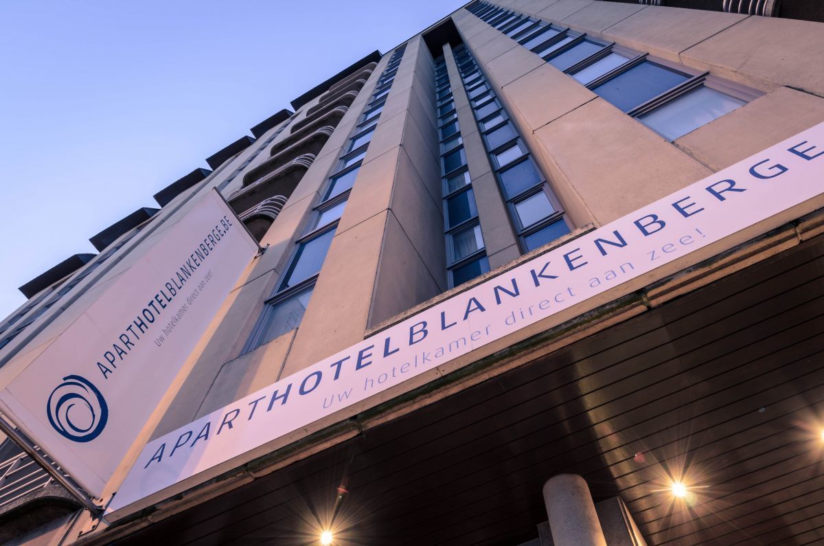 A building with signage for 'APARTHOTELBLANKENBERGE' and 'Uu hotelkamer direct aan zee!' indicating a hotel with direct sea access.