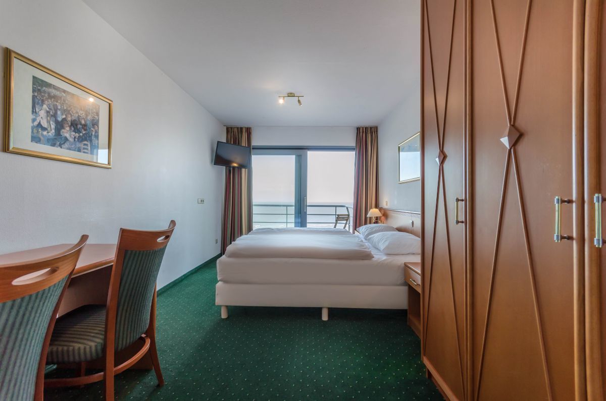 Hotellihuone, jossa on sänky, työpöytä tuolilla, televisio ja suuri ikkuna, jossa on verhot.