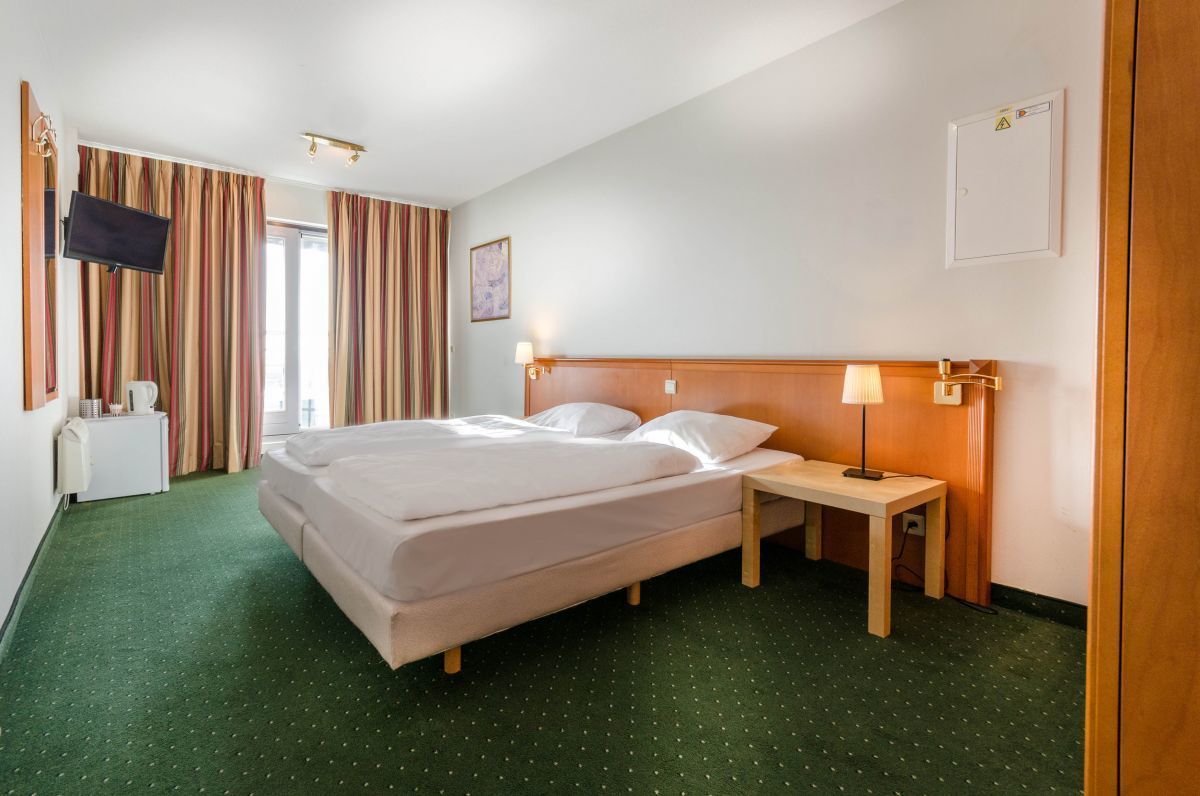 Une chambre d’hôtel avec un lit, une table de chevet, une lampe, une télévision et des rideaux.