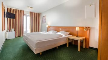 Une chambre d’hôtel avec un lit, une table de chevet, une lampe, une télévision et des rideaux.