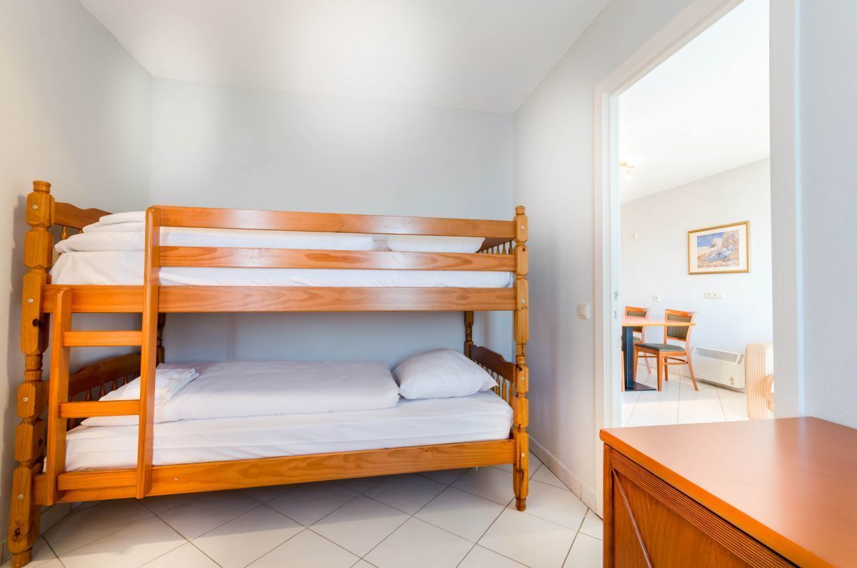 Una cama litera con ropa de cama blanca en una habitación con paredes blancas y suelo de baldosas.