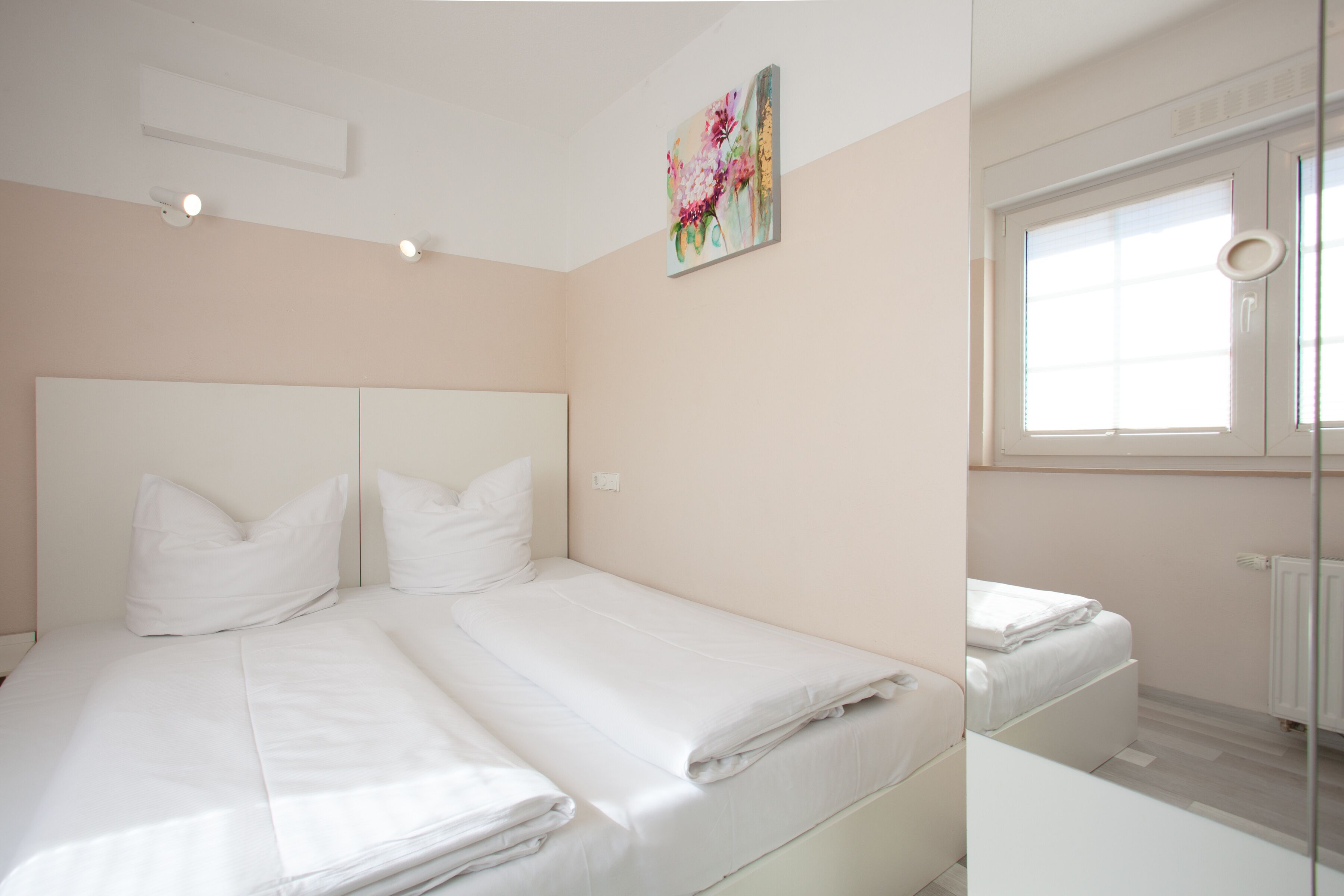 A bedroom with two beds, a window, and a painting on the wall.