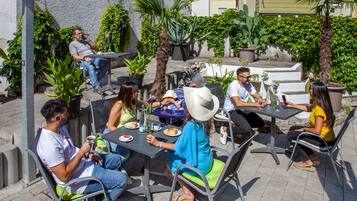 An outdoor café with tables and chairs, surrounded by potted plants and a stone wall.