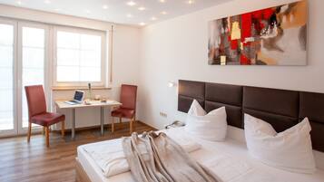 A hotel room with a bed, a desk with a laptop, two chairs, and a large abstract painting on the wall.