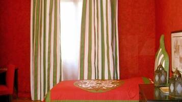 Una stanza con un letto, pareti rosse, tende verdi e una testiera decorativa.
