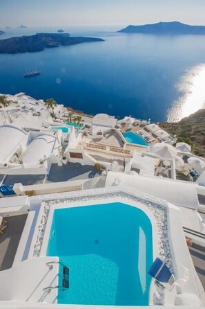 Un resort con una gran piscina rodeada de edificios blancos, con vista a un mar tranquilo y a islas distantes.