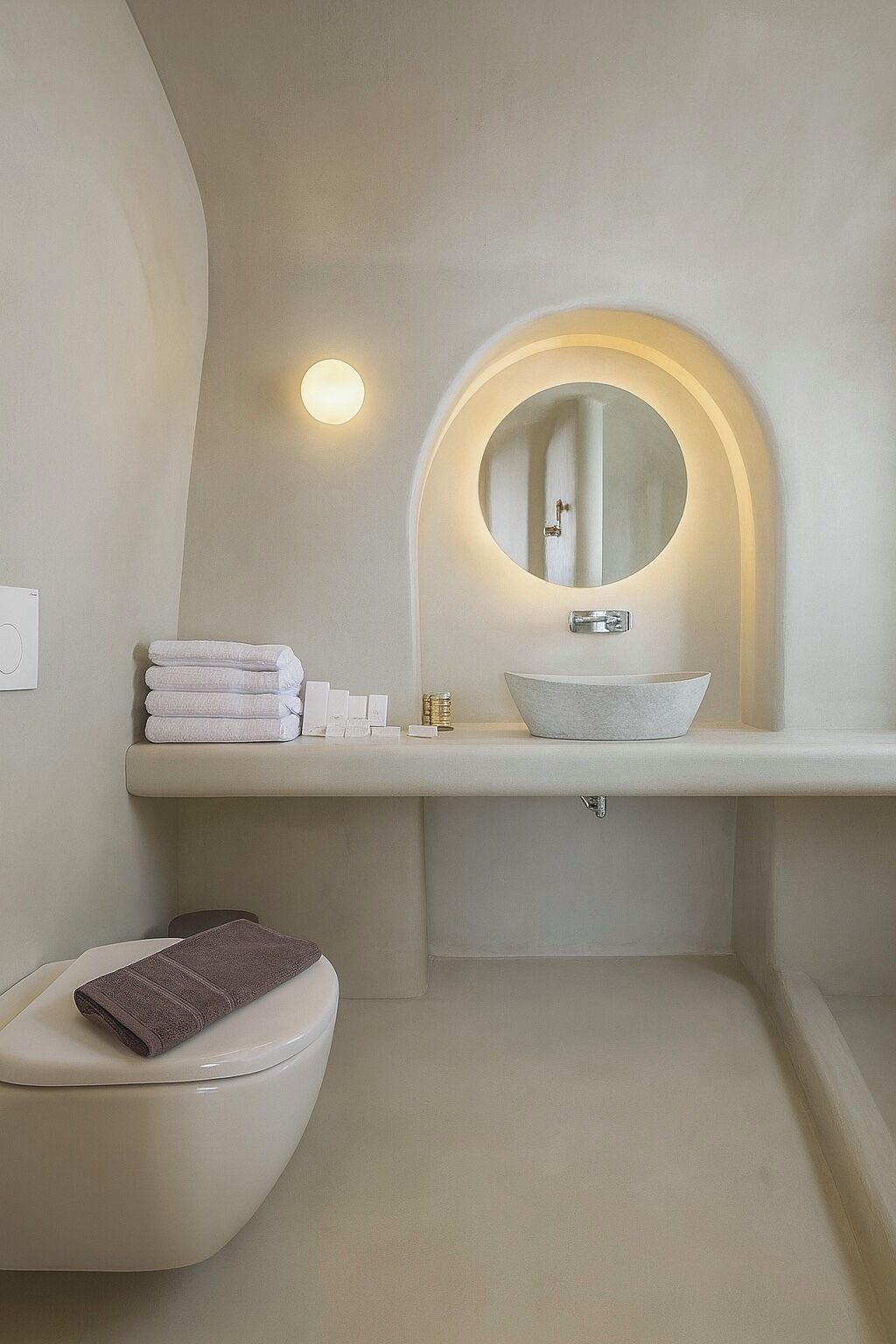 A modern bathroom with a round mirror, white sink, and a toilet.