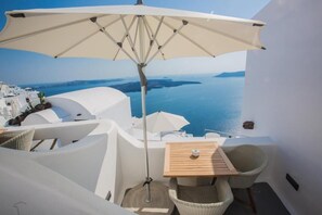 Un balcón con mesa de madera y sillas de mimbre, con vistas panorámicas al mar y a islas distantes.