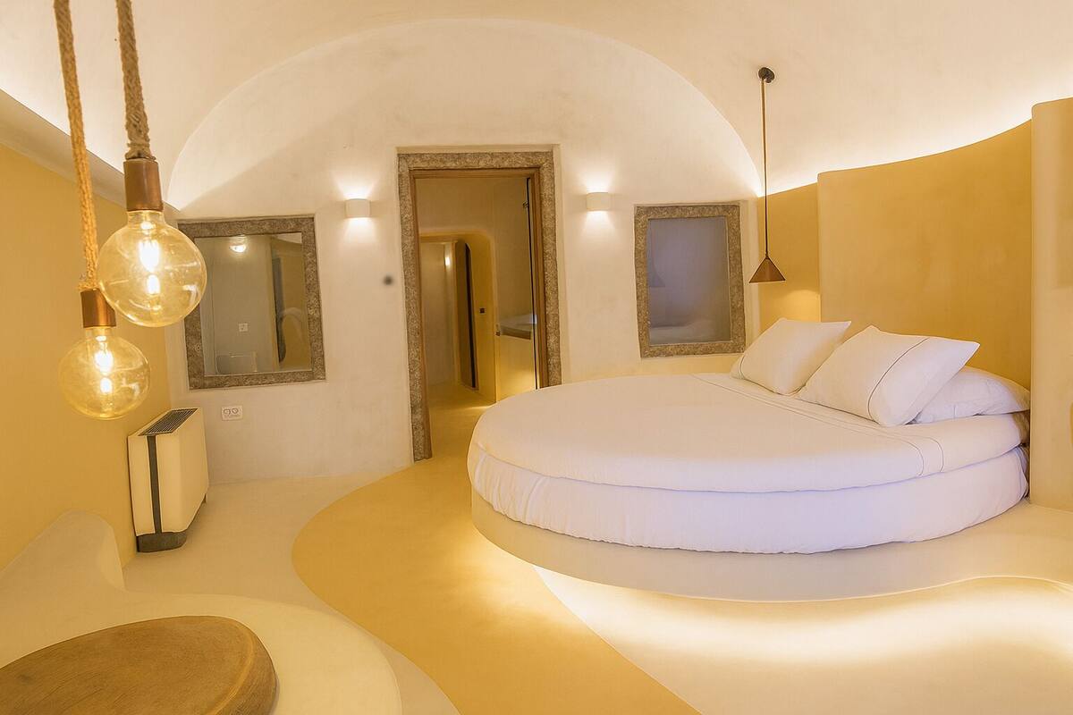 A circular bed in a room with a curved wall, a mirror, and a hanging light fixture.