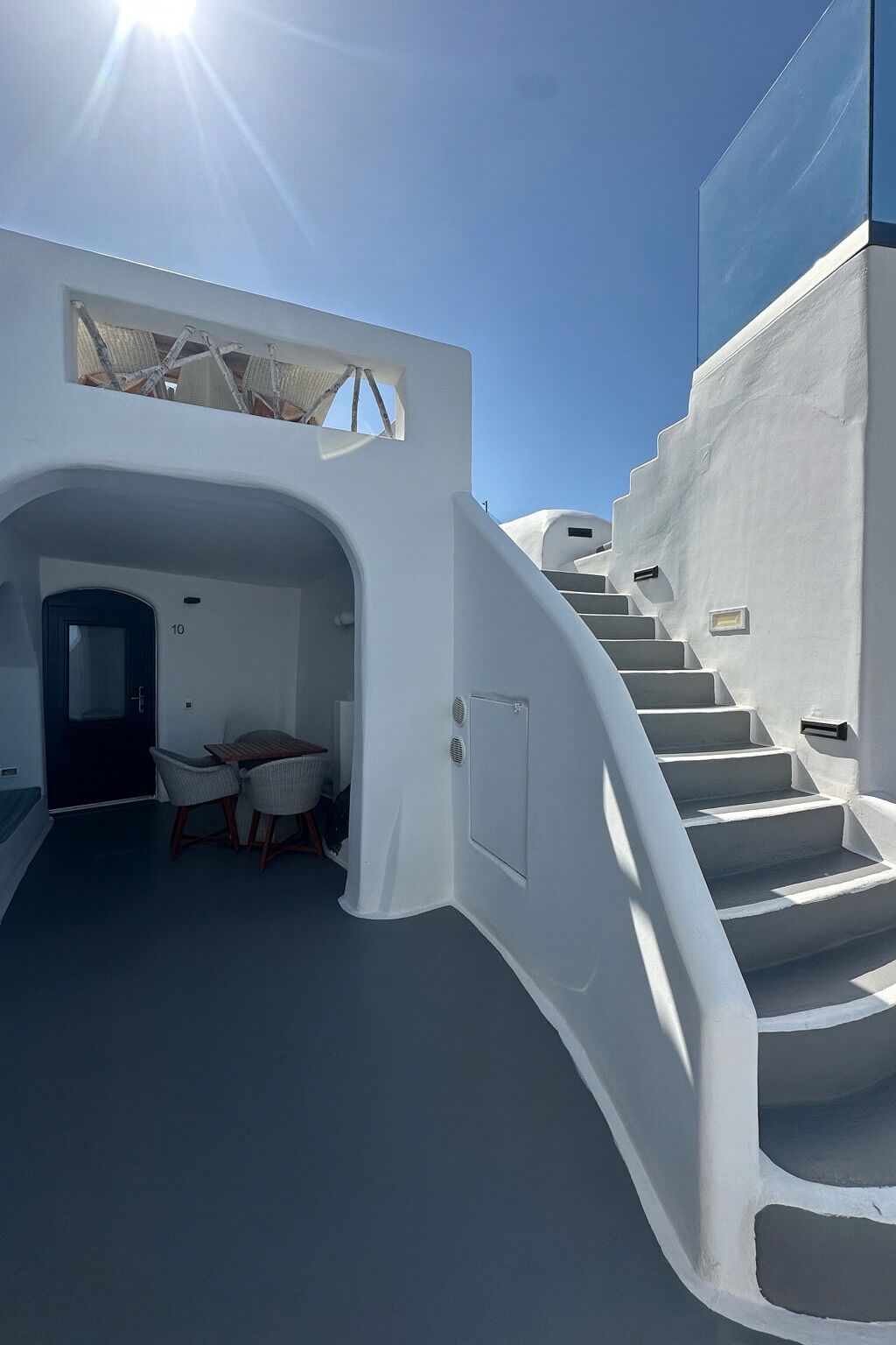 A white building with a staircase leading to a covered area with a table and chairs.