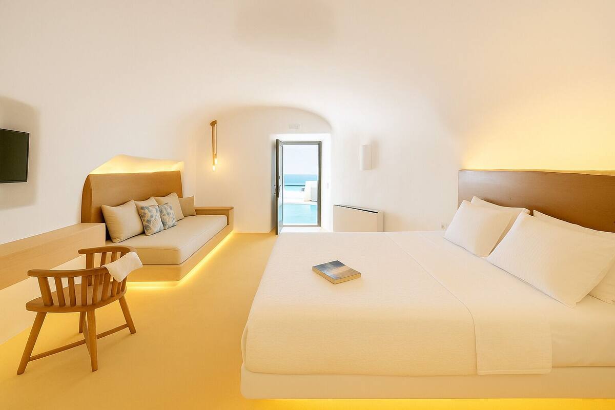 A modern hotel room with a large bed, a sofa, a wooden chair, and a small table.