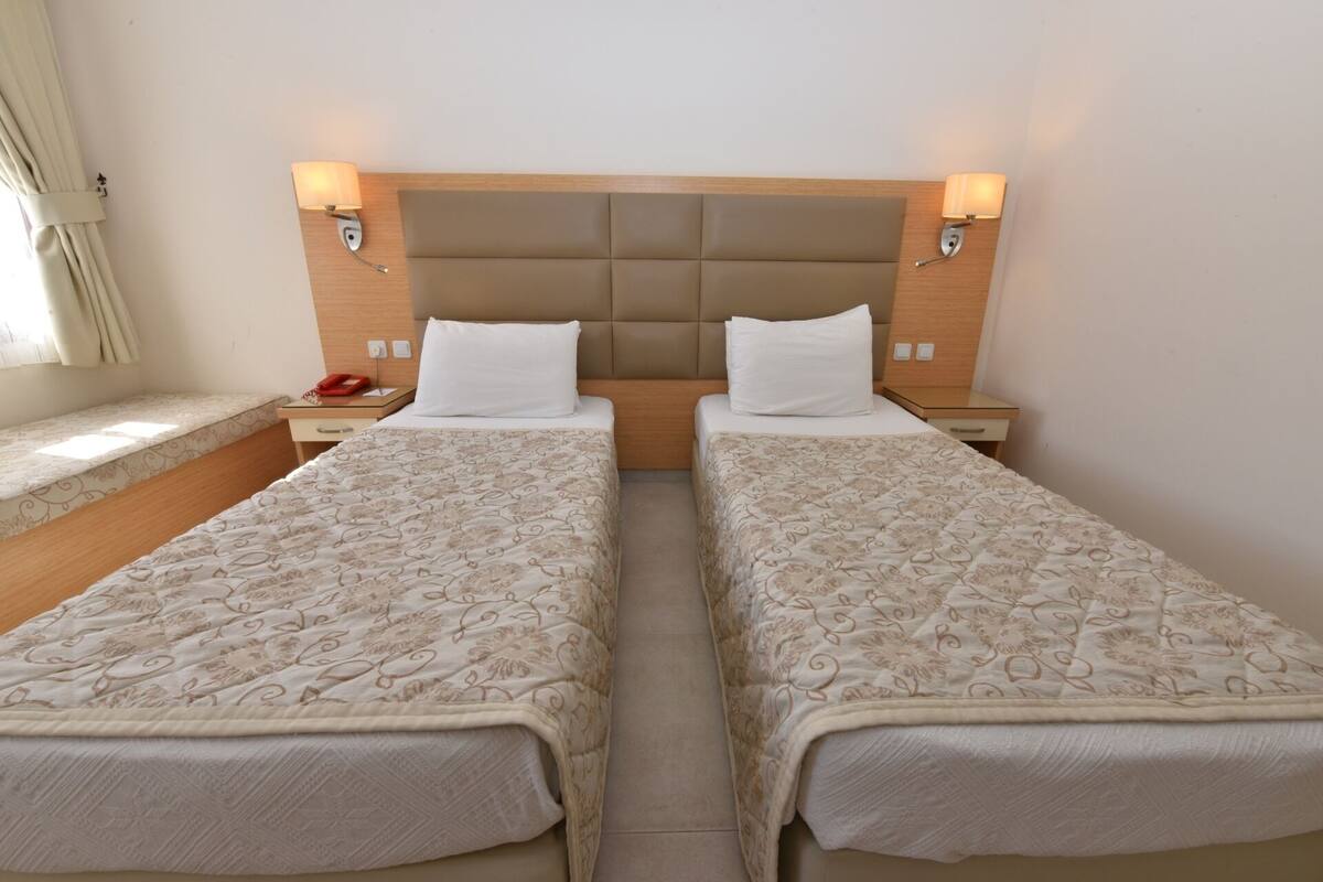 A double bed room with a headboard, bedside tables, lamps, and a window with curtains.