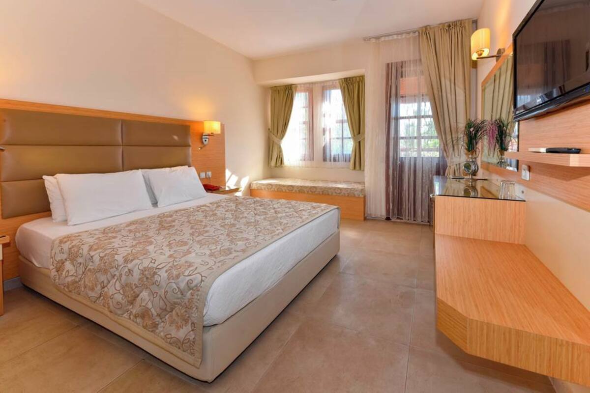Habitació d'hotel amb un llit gran, una taula de treball, una televisió i una finestra amb cortines.