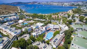 An aerial view of a coastal residential area with a swimming pool, multiple buildings, and a marina in the background. - Flora Hotel Bodrum  (Bodrum)