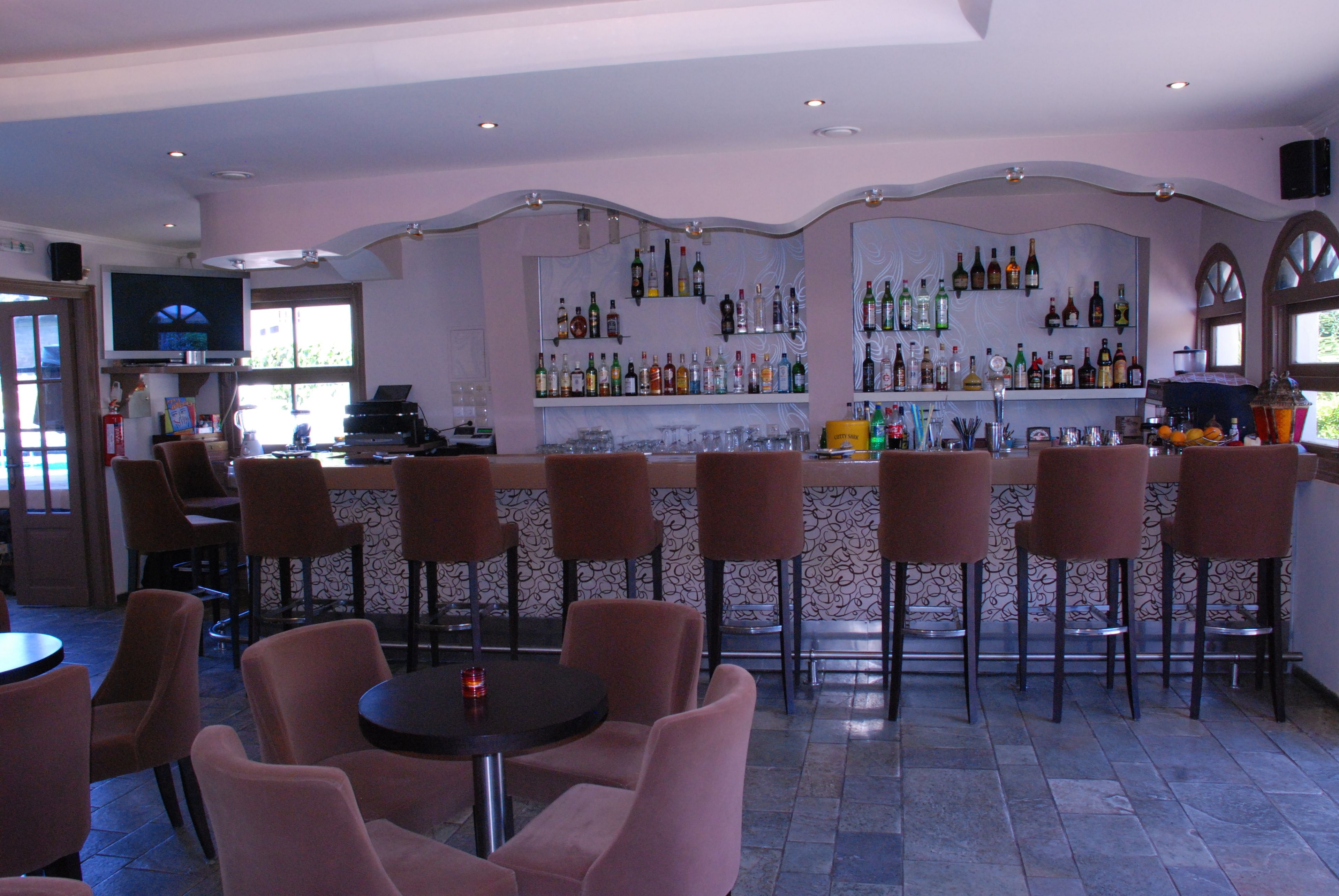 A bar area with multiple seating options, a television, and shelves stocked with various bottles.