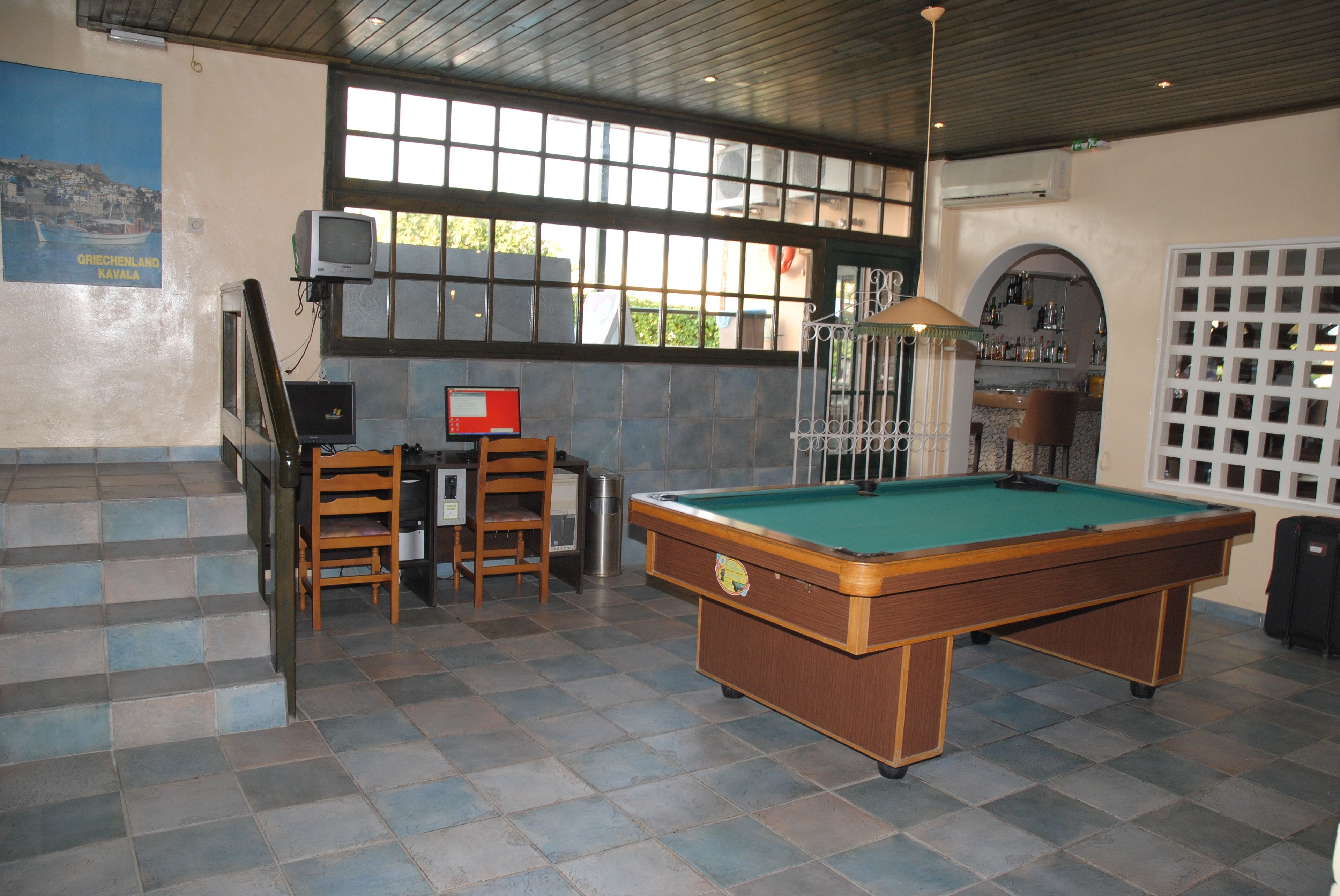 A pool table in a room with a view of the outdoors, a computer, and a poster on the wall.