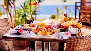 Una mesa de desayuno con platos de comida, una cesta de fruta y un vaso de zumo de naranja.