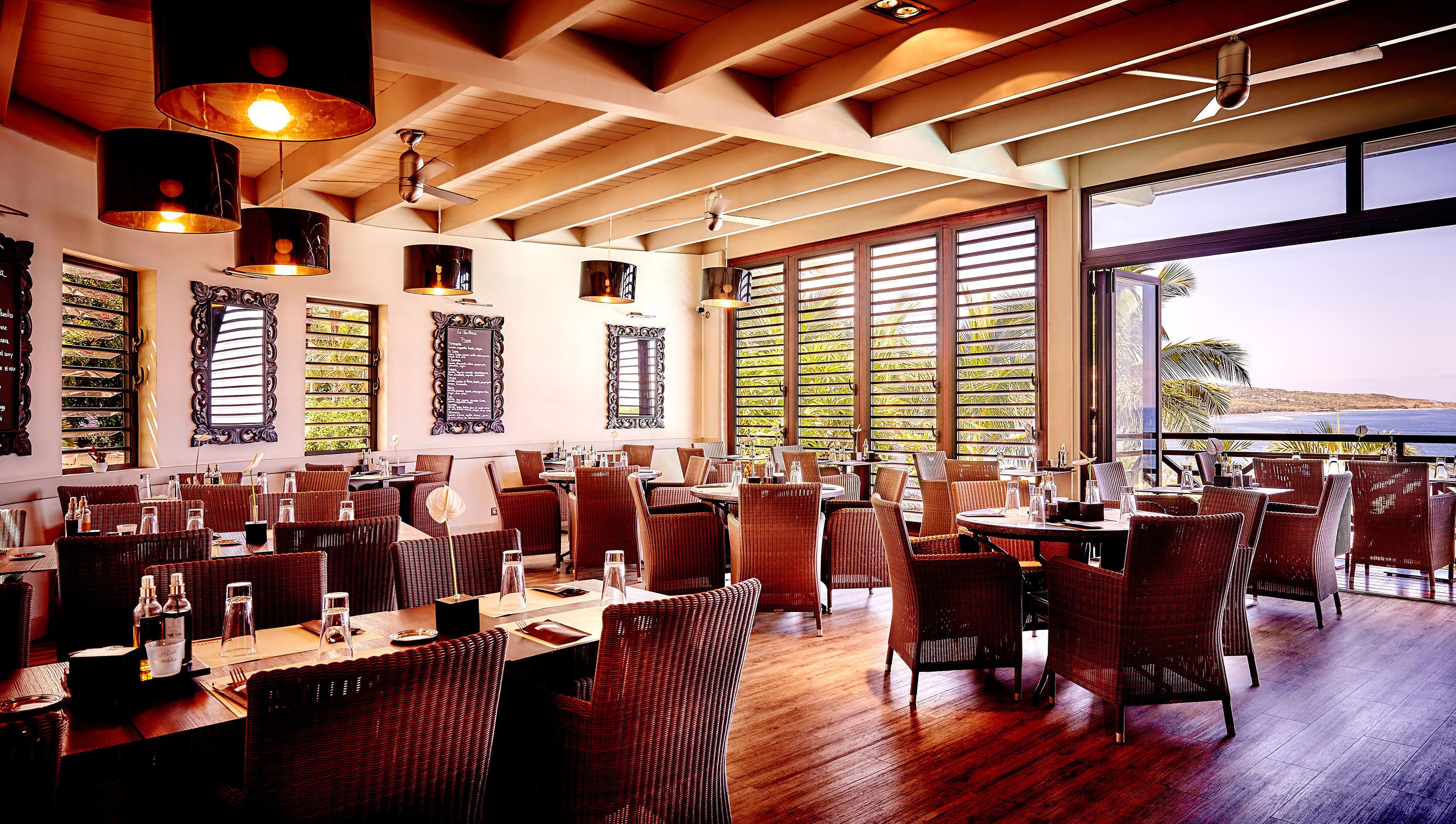 Un restaurante con suelos de madera, sillas de mimbre y grandes ventanales con vistas al mar.