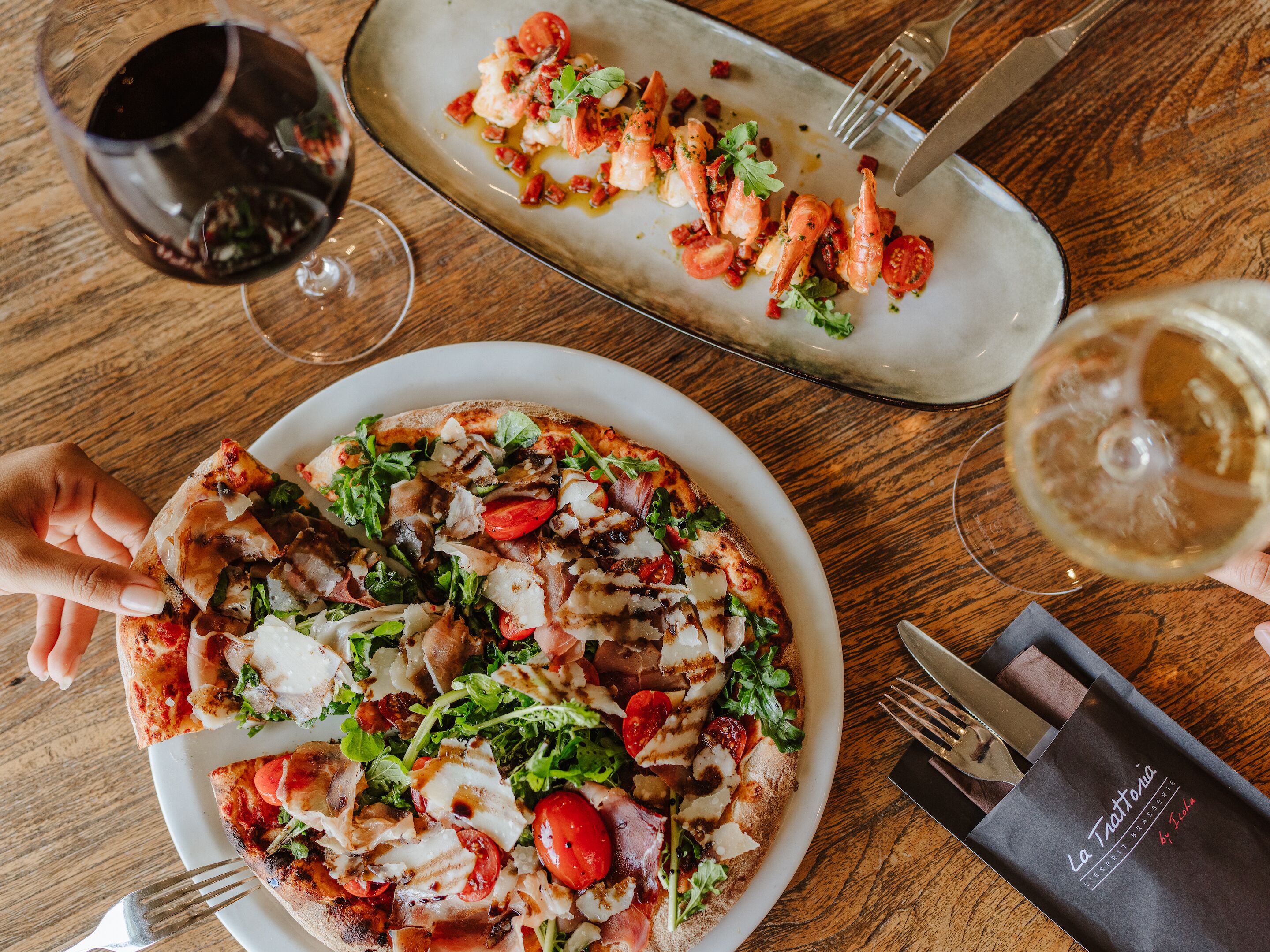 Una mesa de comedor con pizza, una copa de vino tinto y un plato de comida.