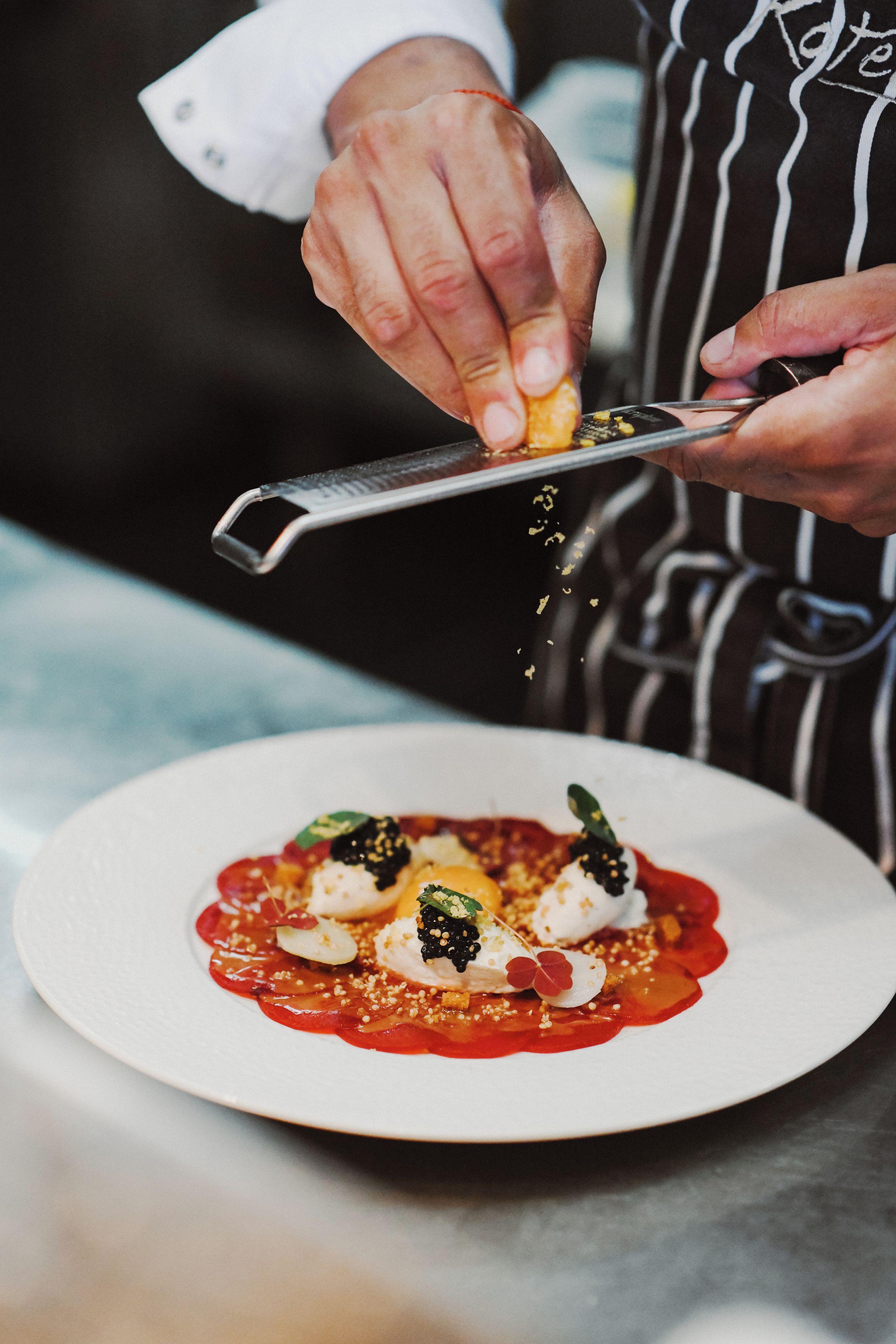 A chef's hands using a knife to prepare a dish on a white plate.