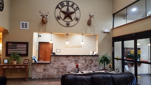 A reception area with a stone counter, American flag, and Texas state emblem. - Velkommen Inn (Clifton)