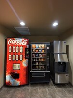 Máquina expendedora con Coca-Cola, diversas opciones de snacks, un dispensador de agua y un refrigerador.