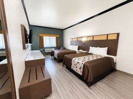 Habitación de hotel con escritorio, dos camas, televisor y ventana con cortinas.